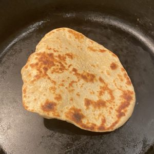 A piece of flatbread cooking in a black skillet.